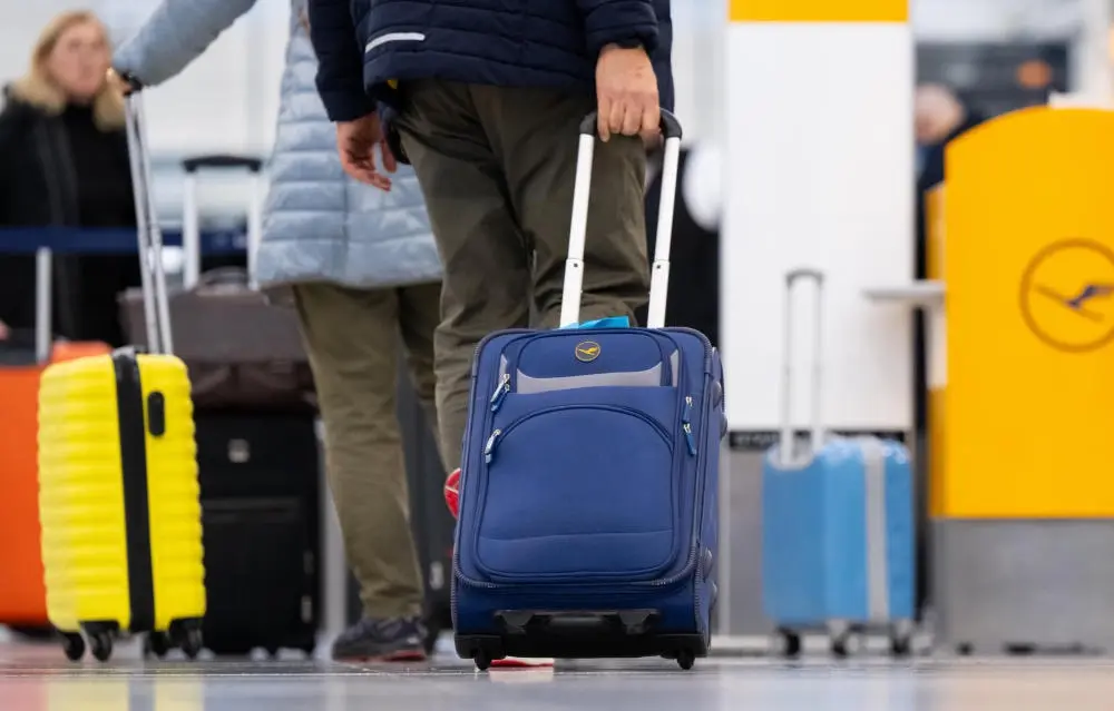 Passagiere stehen mit ihrem Handgepäck am Check-in-Schalter vom Flughafen.