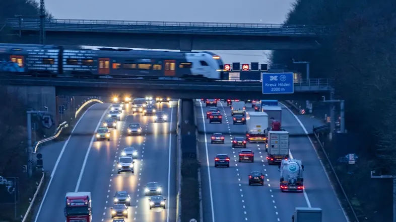 Abendlicher Berufsverkehr auf der A3. Ein Nahverkehrszug überquert die Autobahnbrücke.