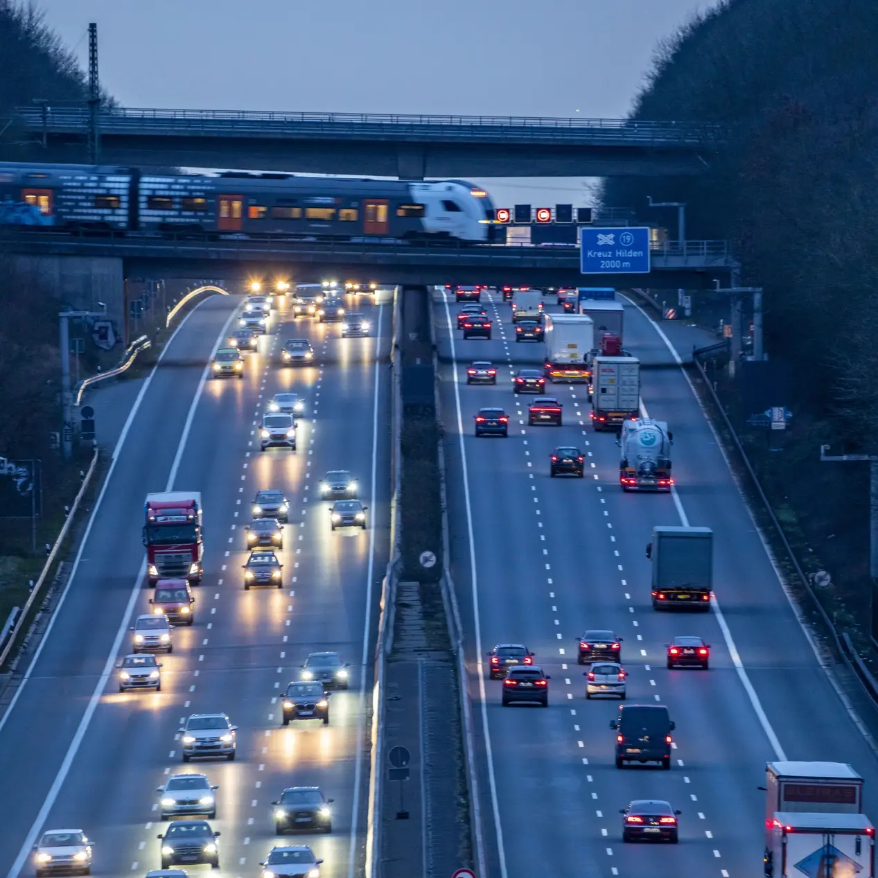 Abendlicher Berufsverkehr auf der A3. Ein Nahverkehrszug überquert die Autobahnbrücke.