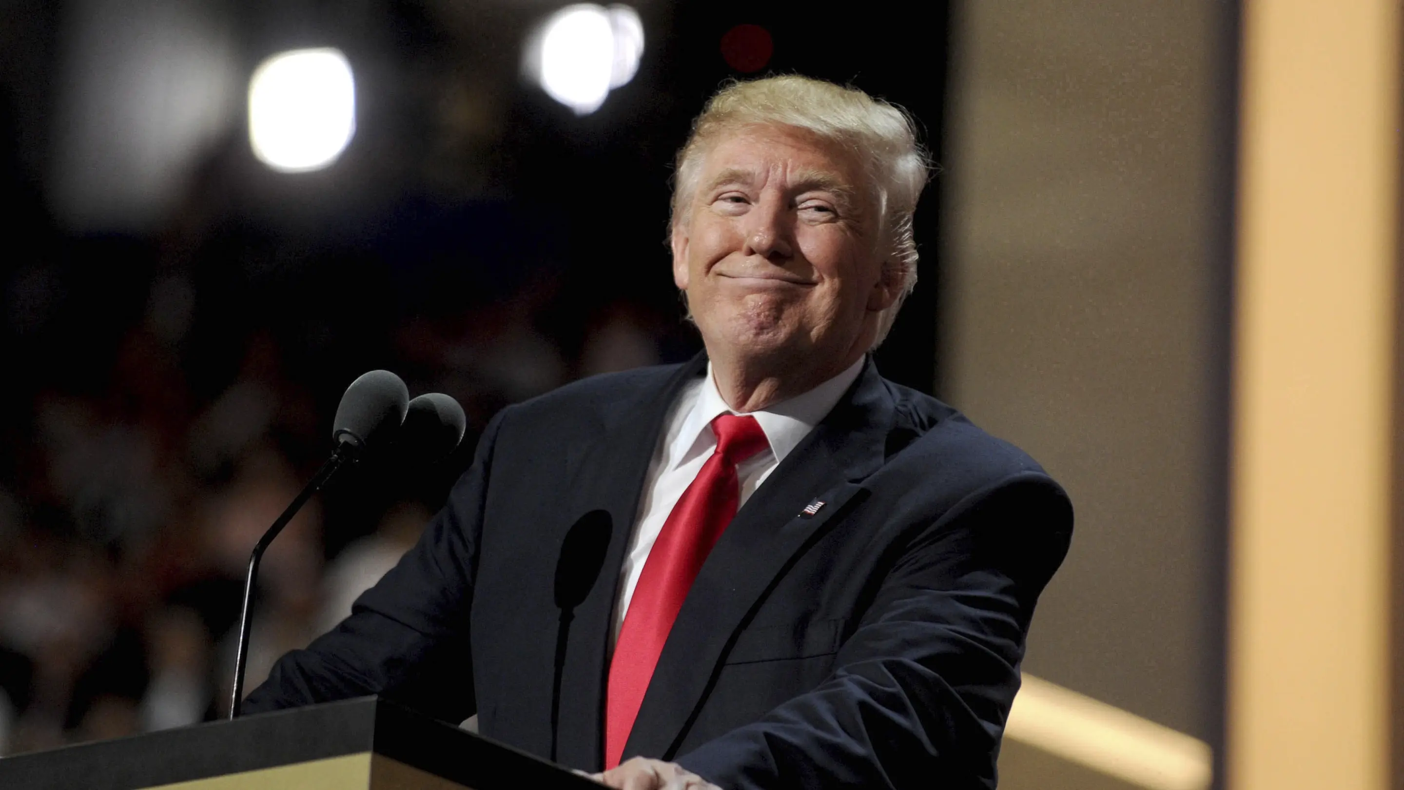 Donald Trump steht grinsend an einem Rednerpult