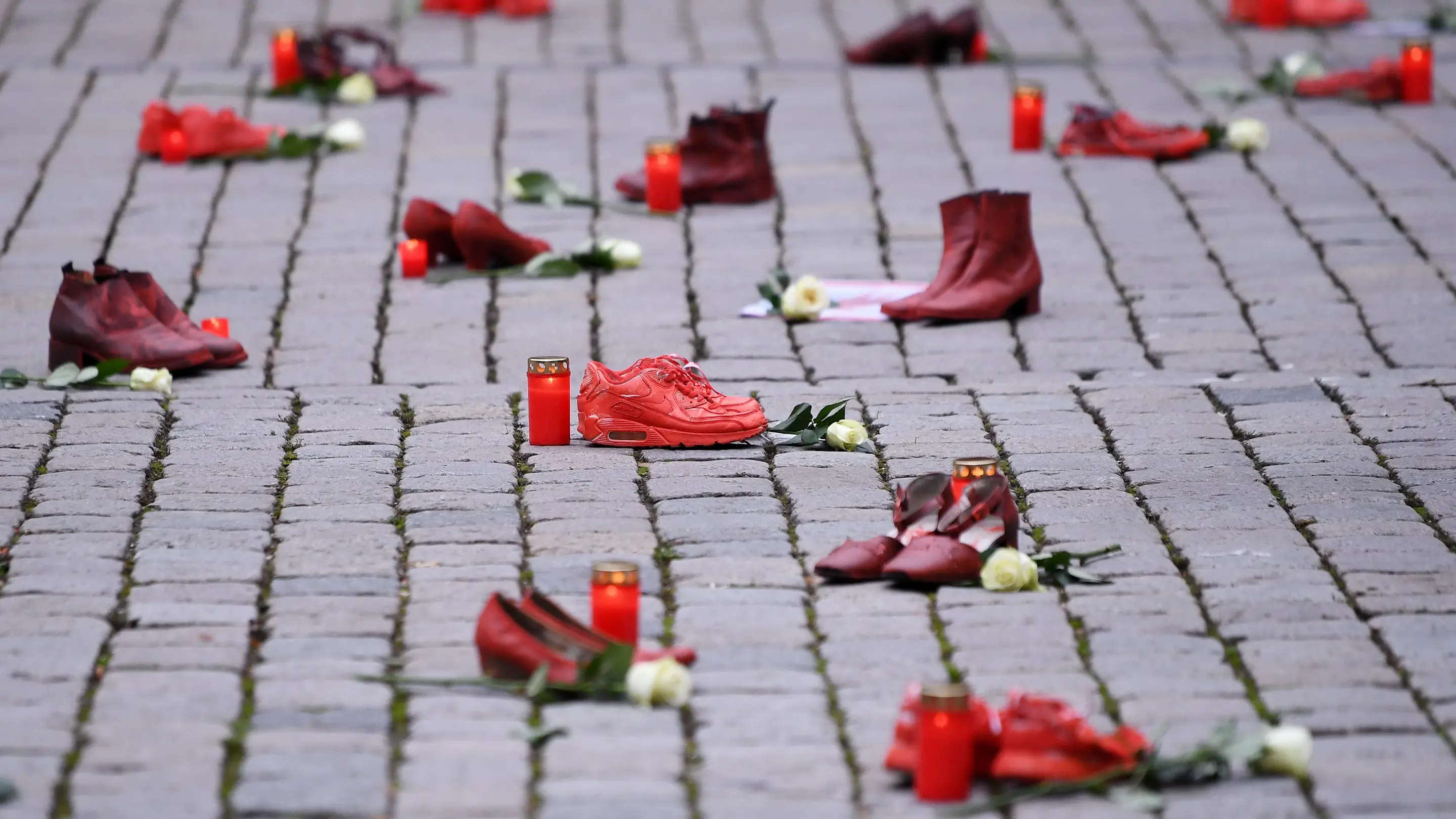 Rote Schuhe mit Grablichtern und weißen Rosen auf einem Gehweg