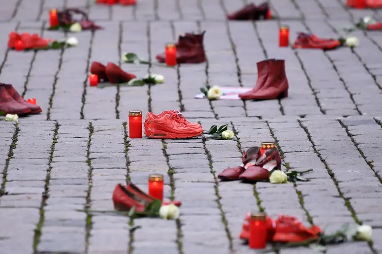 Rote Schuhe mit Grablichtern und weißen Rosen auf einem Gehweg