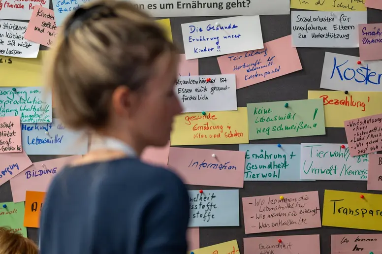 Eine Teilnehmerin des Bürgerrats, graue Pinnwand mit beschrifteten bunten Karten im Hintergrund