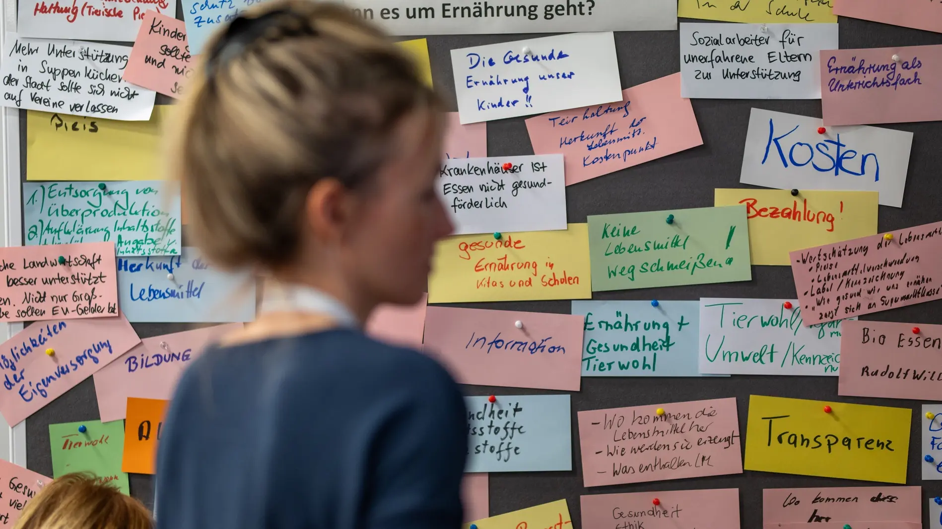 Eine Teilnehmerin des Bürgerrats, graue Pinnwand mit beschrifteten bunten Karten im Hintergrund