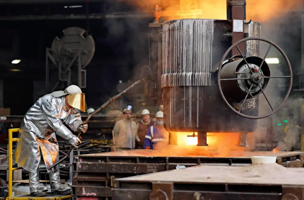 Stahlarbeiter mit Schutzkleidung vor einem Schmelzofen in der Gießerei eines Stahlwerkes.
