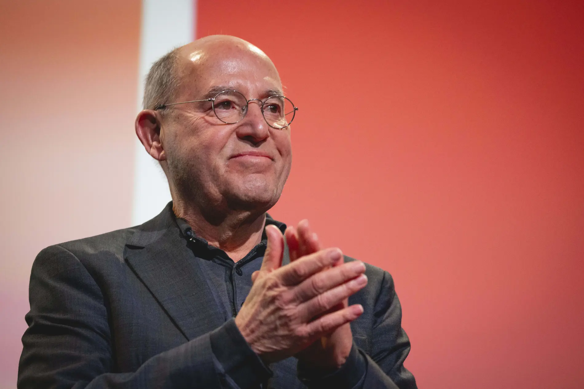 Gregor Gysi klatscht in die Hände vor einer roten Wand