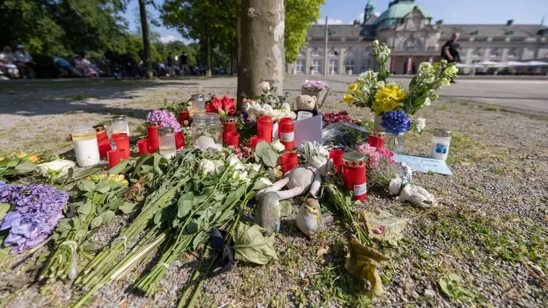 Blumen, Kerzen und handgeschriebene Trauerbekundungen stehen an einem Baum im Kurpark Bad Oeynhausen.
