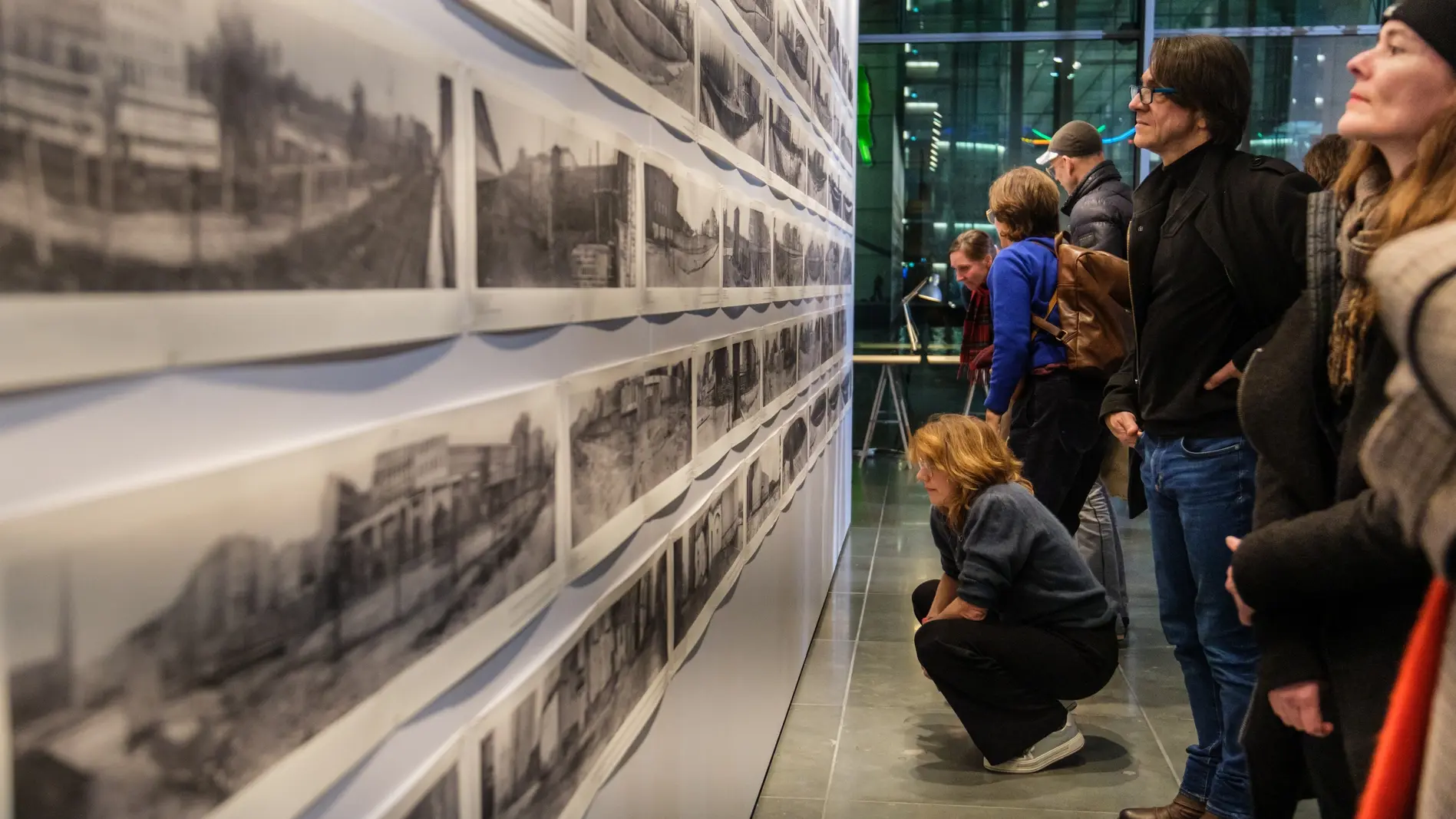 Besucher der Ausstellung blicken auf Bilder der Berliner Mauer