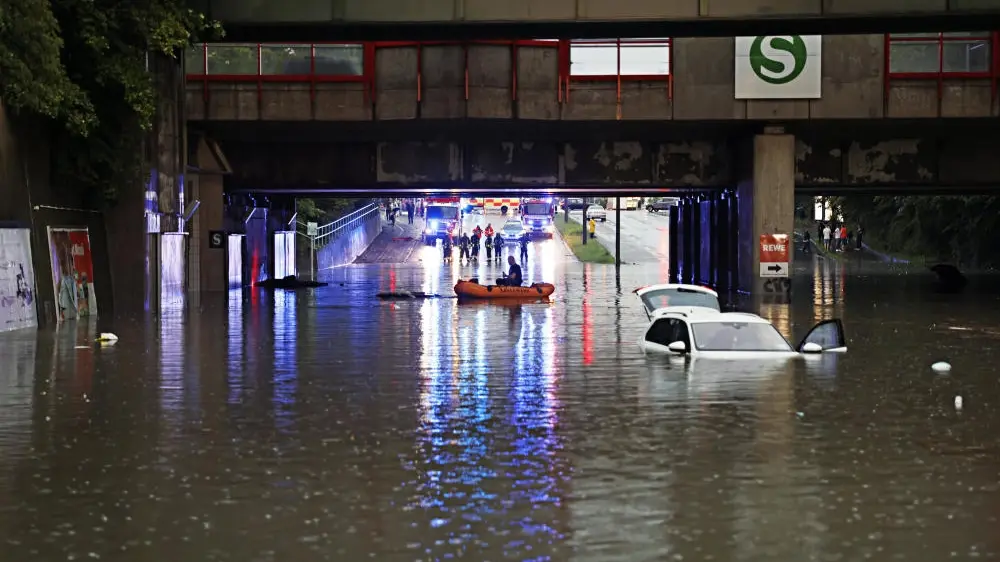 Durch Starkregen überschwemmte Straße; ein Auto ist fast komplett versunken.