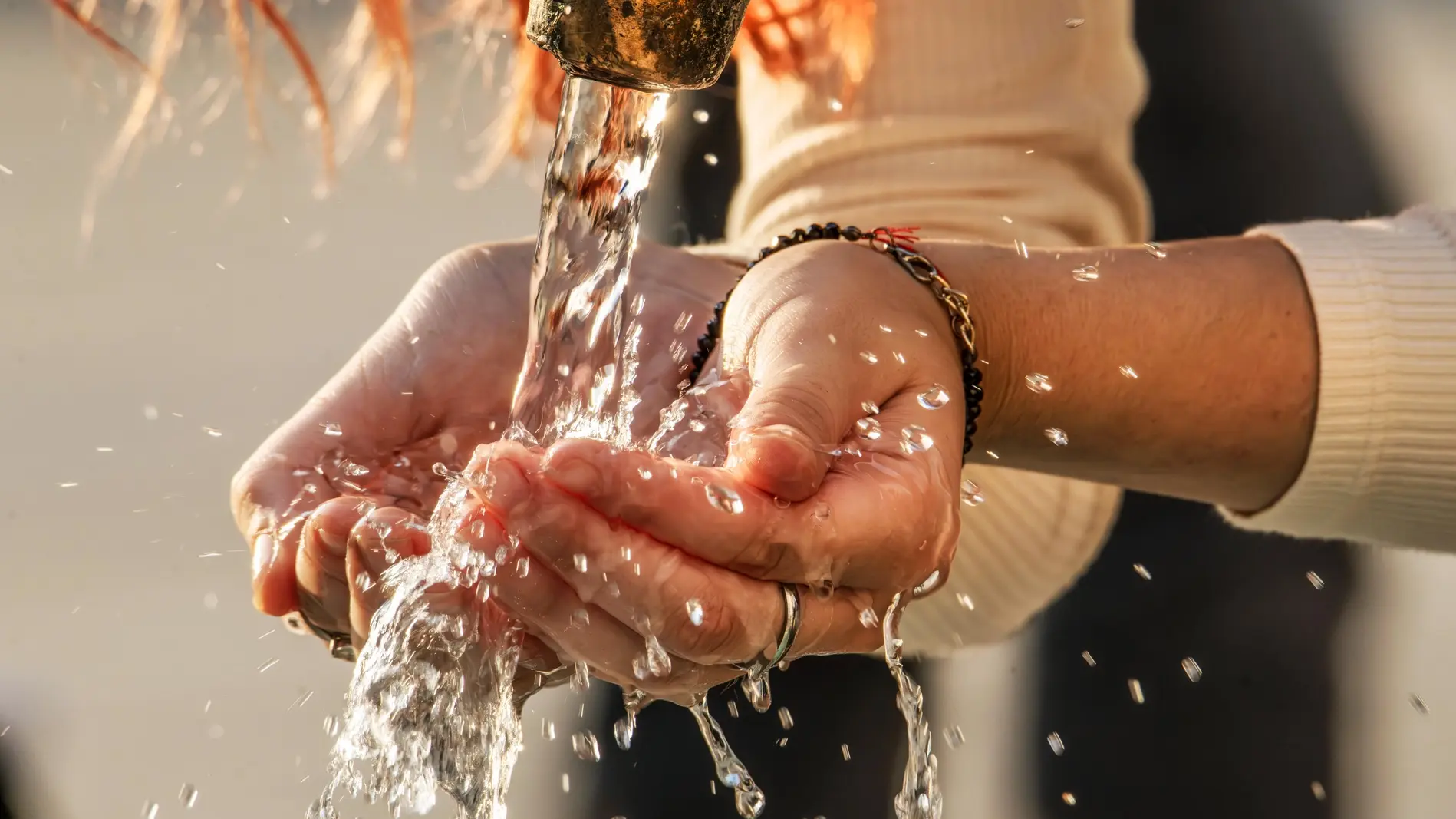 Frau schöpft mit ihren Händen Trinkwasser aus einem Brunnen