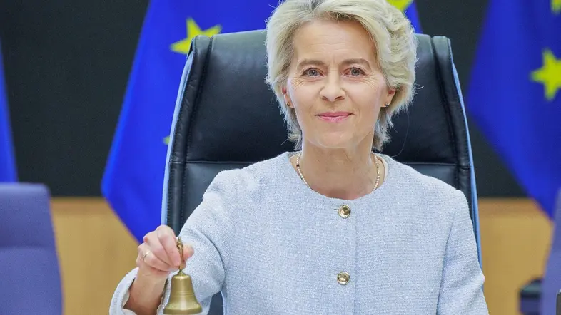 Ursula von der Leyen mit Glocke vor EU-Flaggen