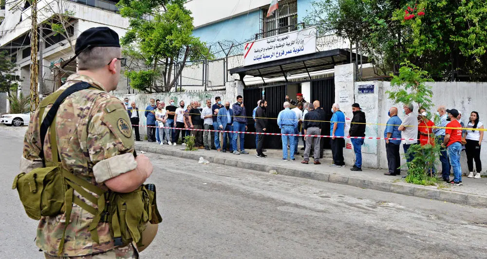 Menschen stehen in einer Schlange vor einem Wahlbüro im Libanon. Im Vordergrund steht ein libanesischer Soldat.