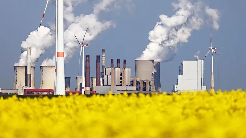 Windräder von RWE drehen sich am Tagebau Garzweiler vor dem Kraftwerk Neurath hinter einem Rapsfeld.