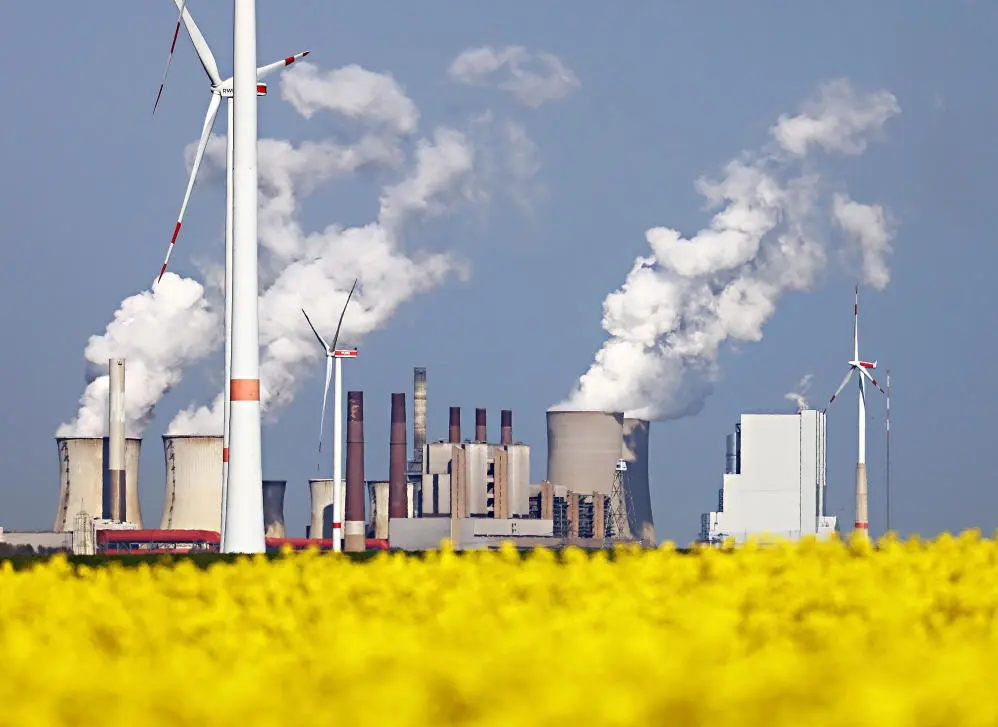 Windräder von RWE drehen sich am Tagebau Garzweiler vor dem Kraftwerk Neurath hinter einem Rapsfeld.