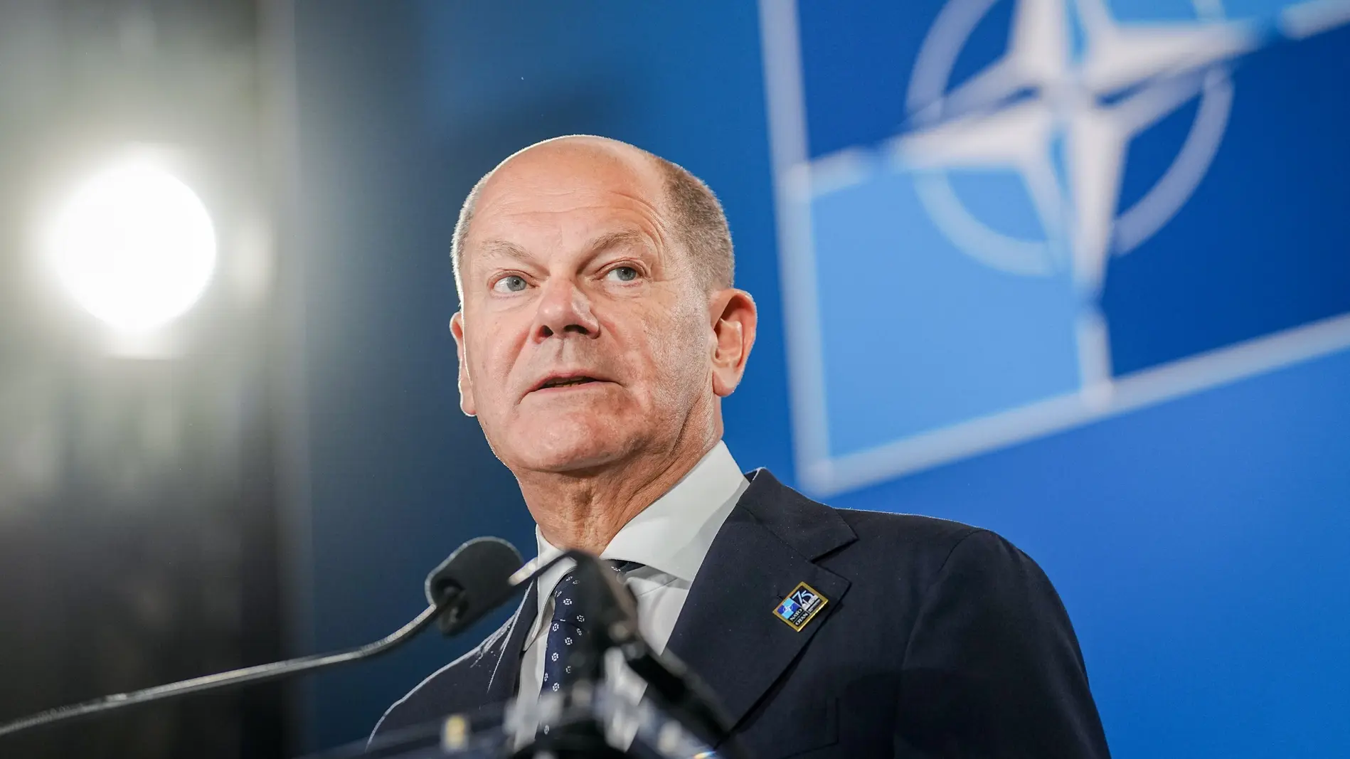 Olaf Scholz vor einer NATO-Flagge