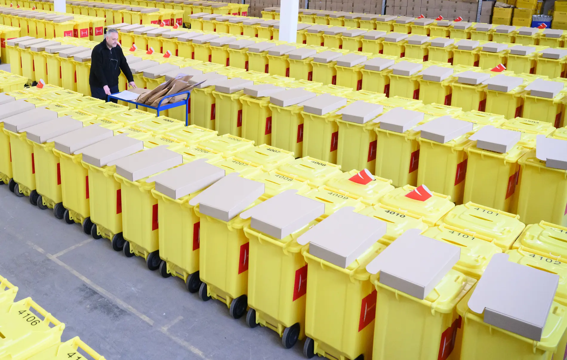 Mann läuft zwischen reihweisen gelben Wahlurnen mit einem Wagen herum