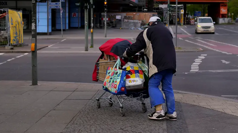 Ein wohnungsloser Mann mit einem voll beladenen Einkaufswagen auf einer Straße