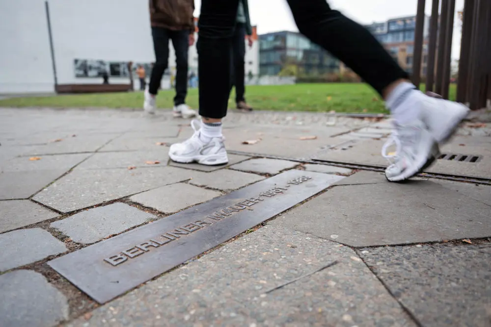 Eine Person überschreitet an der Gedenkstätte Berliner Mauer in der Bernauer Straße den Streifen am Boden, der mit "Berliner Mauer" gekennzeichnet ist deren ehemaligen Verlauf kennzeichnet.