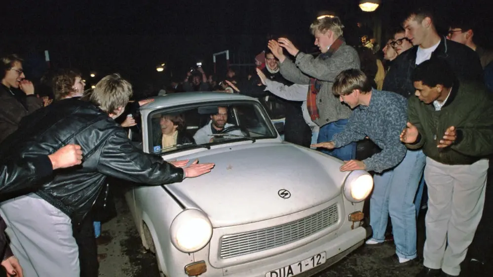 Ein Trabbi wird an der Deutsch-Deutschen Grenze von Menschen begrüßt.