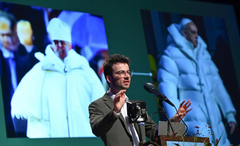 Gregor Schmalzried spricht vor einer Projektion mit KI-generierten Fotos von Papst Franziskus. 