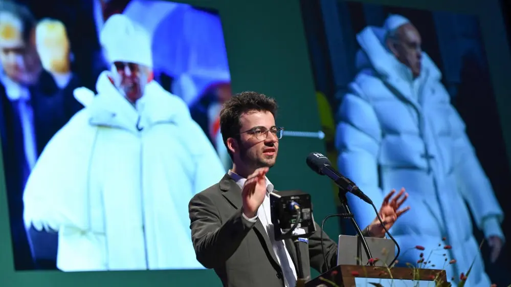 Gregor Schmalzried spricht vor einer Projektion mit KI-generierten Fotos von Papst Franziskus. 