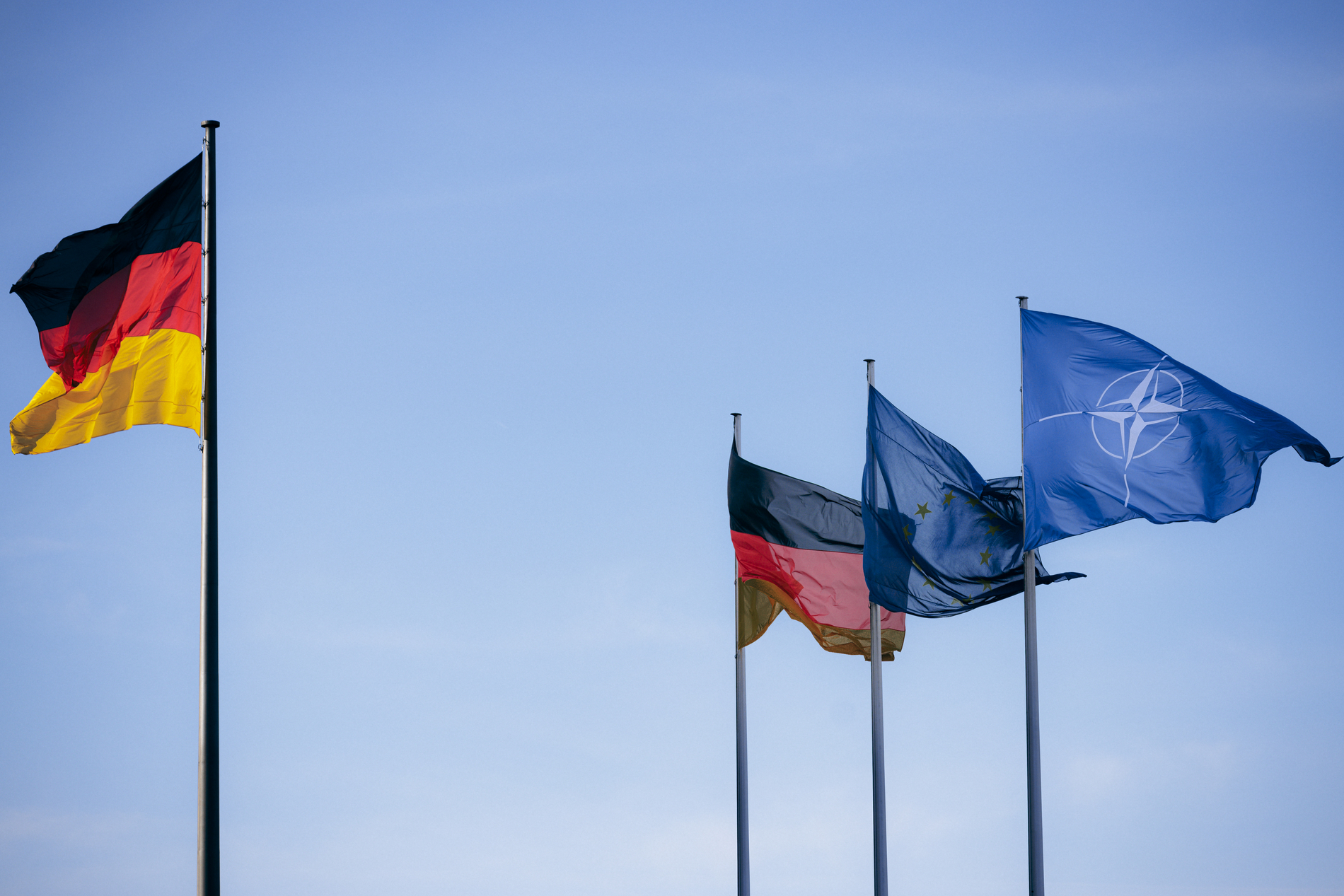Die Deutschland-, EU- und NATO-Flaggen nebeneinander vor dem blauen Himmel